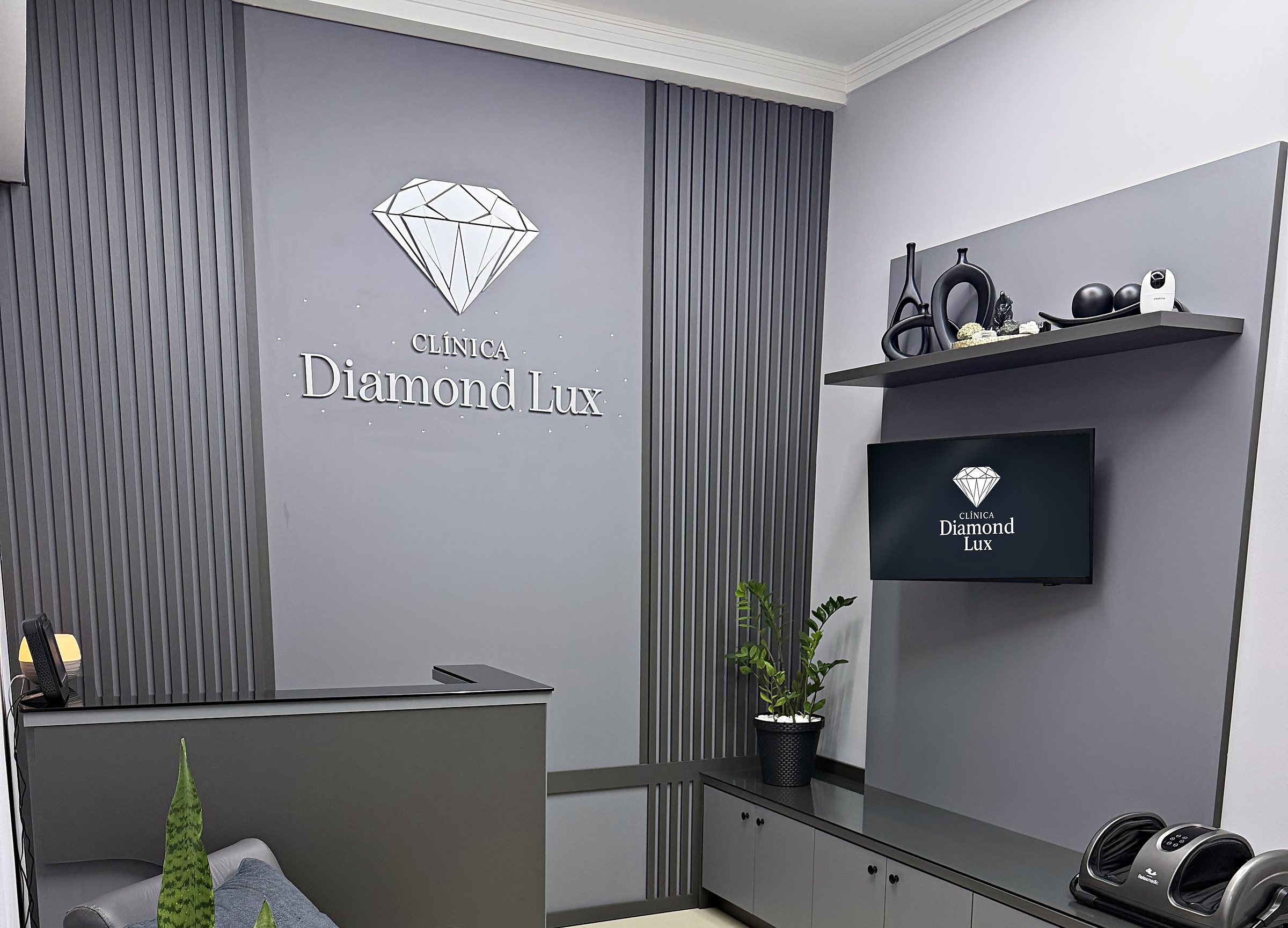 Recepção da Clínica Diamond Lux, com painel ripado, poltronas e televisão.